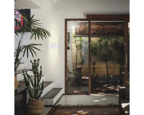 Intérieur avec plantes, escalier et coin repas derrière une porte coulissante en verre.