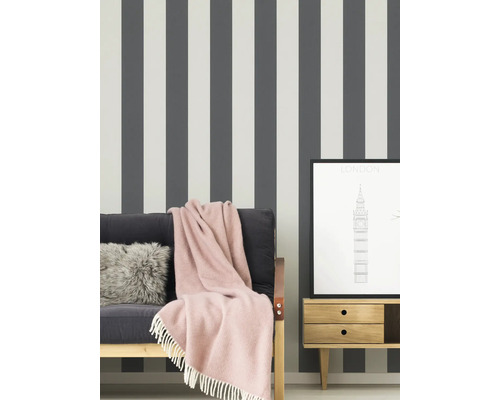 Scène avec papier peint rayé, canapé avec couverture, coussin et une gravure de Londres encadrée sur une table de chevet.