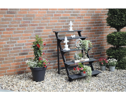 Espace de jardin décoratif avec étagère à plantes, fleurs et objets ornementaux devant un mur de briques.