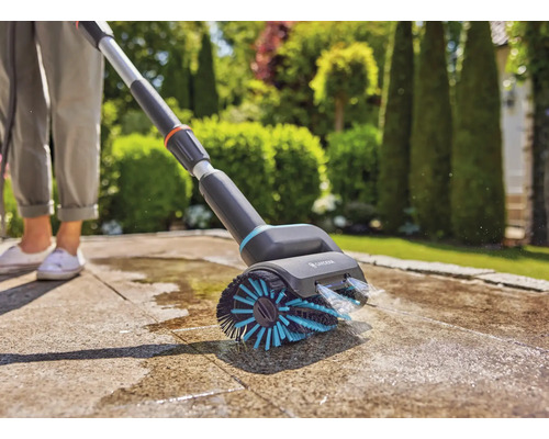 Nettoyeur de surfaces Gardena avec brosse et raccord d''eau en utilisation sur une terrasse.