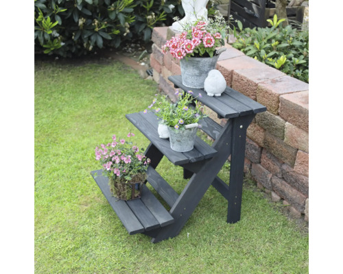 Schwarzes Blumenregal aus Holz mit drei Ebenen im Garten mit Blumenarrangements.