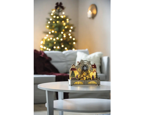 Dekorative hölzerne Weihnachtsbeleuchtung mit Riesenrad auf einem Tisch, im Hintergrund ein Weihnachtsbaum