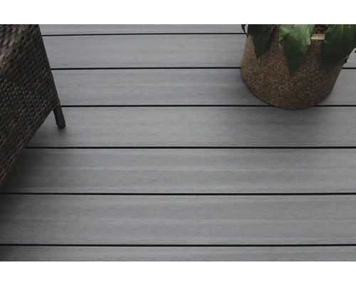 Gros plan d''une terrasse avec des planches en bois, un fauteuil en rotin et un pot de fleurs.