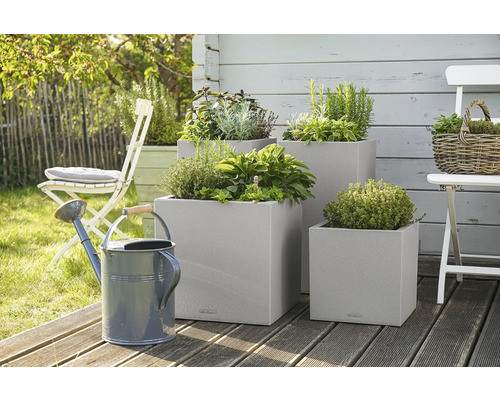 Drei quadratische Pflanzkübel mit Kräutern und eine Giesskanne im Garten