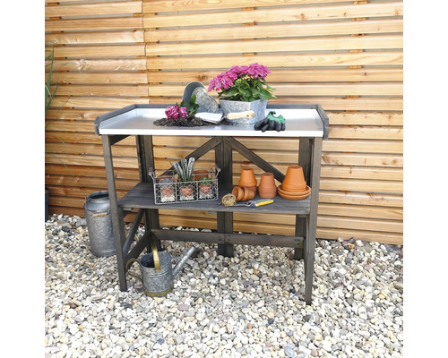 Table de jardin avec plan de travail, fleurs, outils et pots devant une clôture en bois