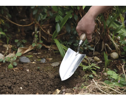 Jardinier plantant avec une plantoir dans le jardin.