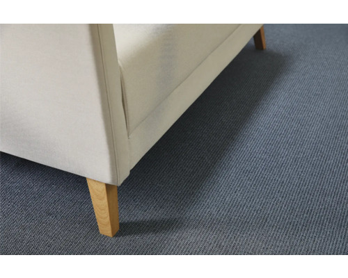 Detailansicht eines Polstermöbels mit Stoffbezug und Holzfüßen auf einem Teppichboden.
