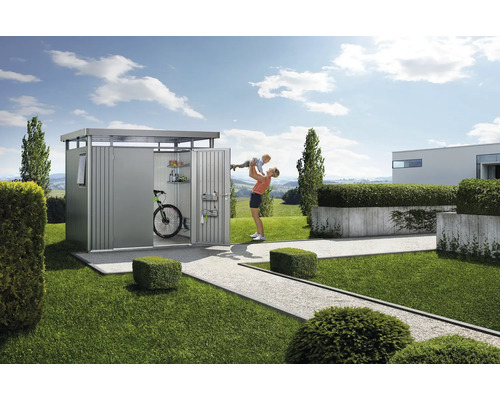 Gartenszene mit Geräteschuppen, Fahrrad, Regalen und einer Frau, die ein Kind hochhebt