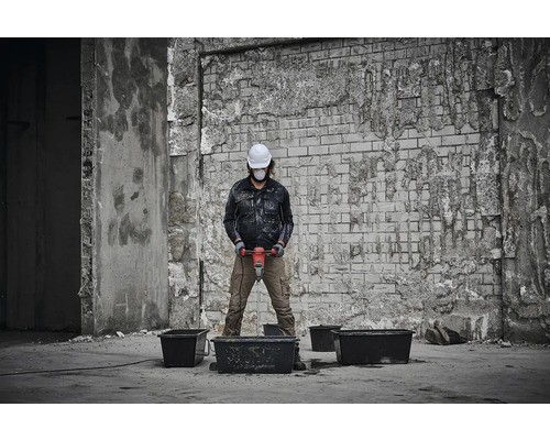 Une personne portant un casque de sécurité et un masque de protection mélange des matériaux avec un mélangeur dans un environnement de construction.