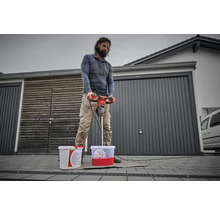 Un homme mélange de la peinture avec un mélangeur de peinture devant un garage
