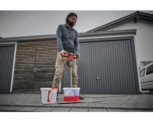 Un homme mélange de la peinture avec un mélangeur de peinture devant un garage