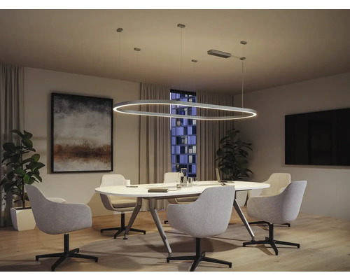 Salle de conférence moderne avec suspension ovale au-dessus d''une table ronde avec des chaises.