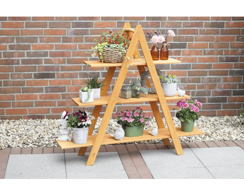 Échelle décorative «Maxi» en bois 137 x 31 x 120 cm couleur miel Étagère à plantes en bois avec trois niveaux et diverses plantes en pot devant un mur de briques