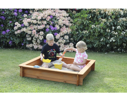Zwei Kinder spielen in einem Holzsandkasten im Garten mit Sandspielzeug.