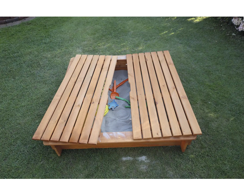 Sandkasten aus Holz mit Deckel und Spielzeug auf Rasen