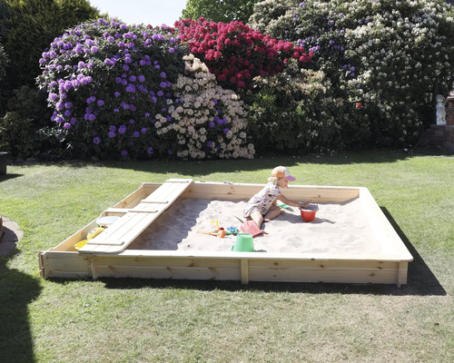 Kind spielt im Sandkasten mit Sandspielzeug im Garten.