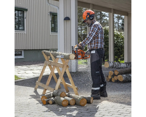 Eine Person sägt mit einer Kettensäge Holz auf einem Holzbock, während sie eine Schutzausrüstung trägt.