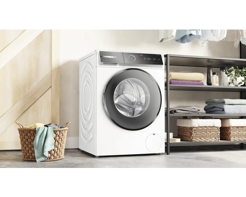 Machine à laver à chargement frontal dans une pièce lumineuse avec un panier à linge et une étagère.