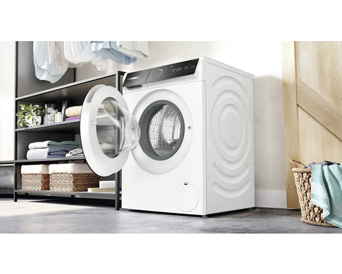 Machine à laver blanche avec porte ouverte dans une buanderie avec étagères et paniers à linge.