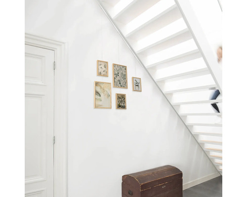 Flur mit weißer Treppe, Holztruhe und hängenden gerahmten Bildern mit Pflanzenmotiven