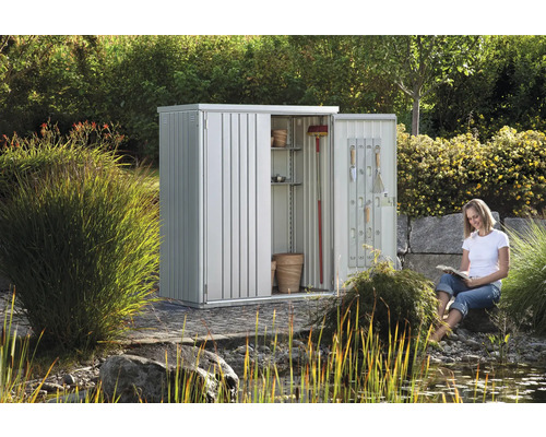 Abri de jardin en métal avec étagères et outils dans le jardin avec une femme qui lit