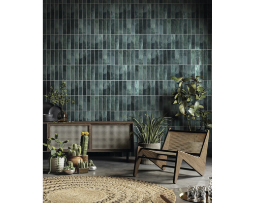 Séjour avec carrelage mural vert, meuble en bois, chaise en rotin et plantes