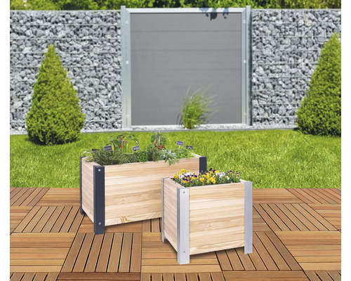 Deux jardinières en bois avec des herbes aromatiques et des fleurs sur une terrasse, avec un jardin et une clôture en arrière-plan.