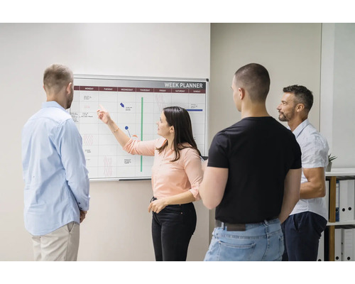Personen, die einen Wochenplaner an einer Wandtafel im Büro besprechen