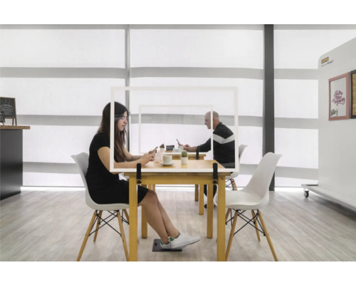 Scène avec deux personnes à des tables séparées par une protection hygiénique transparente