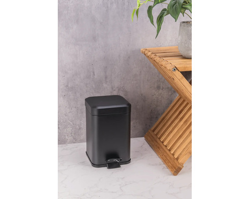 Poubelle à pédale noire en métal à côté d''un tabouret en bois avec une plante