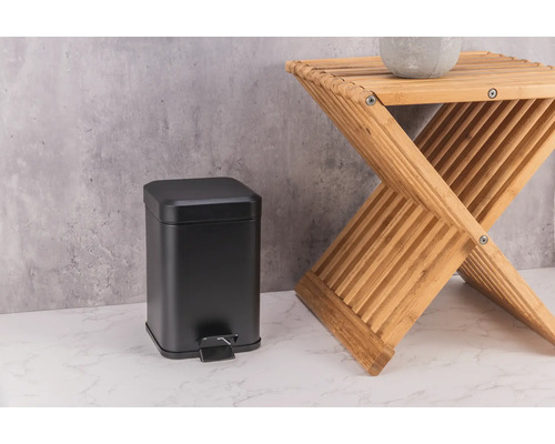 Poubelle à pédale noire en métal à côté d''un tabouret en bois.