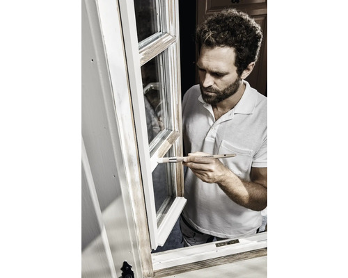 Un homme peint une fenêtre en blanc avec un pinceau.