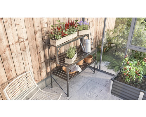 Gartenszene mit dreistufigem Pflanztisch aus Metall, bepflanzt mit Kräutern und Blumen, Giesskanne und Gartenhandschuhen