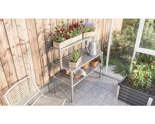 Scène de jardin avec table de plantation, plantes et outils de jardin sur une terrasse à côté d''une serre