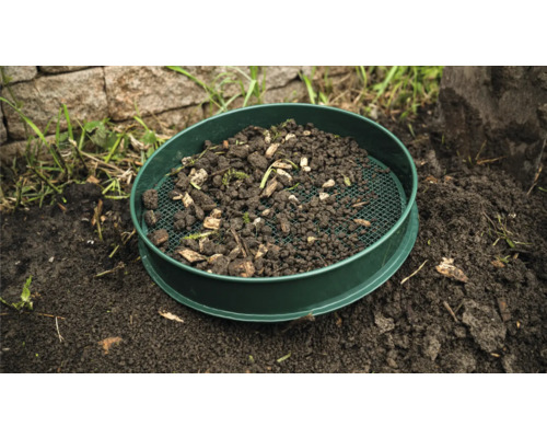 Tamis de jardin avec terre et restes de plantes sur le sol