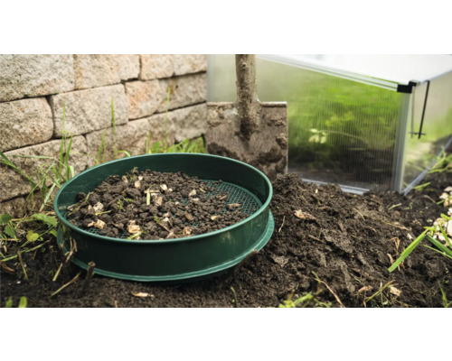 Tamis de jardin avec terre, pelle et serre en arrière-plan