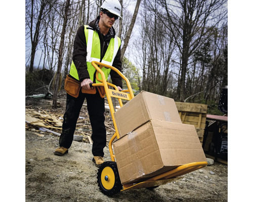 Ein Bauarbeiter transportiert mit einer Sackkarre Kartons auf einer Baustelle. Die Sackkarre ist gelb und trägt das DeWalt Logo.