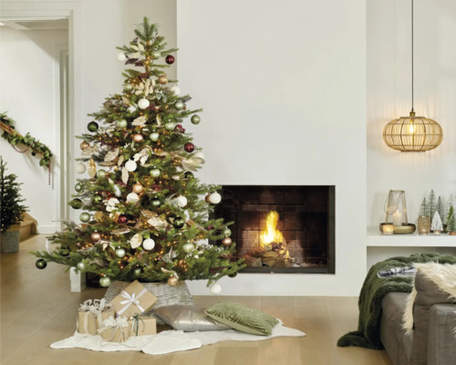Arbre de Noël avec boules, lumières et cadeaux dans un salon avec cheminée.