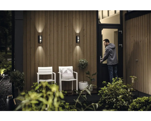 Extérieur d''une maison avec des appliques murales, des chaises et une personne ouvrant une porte.