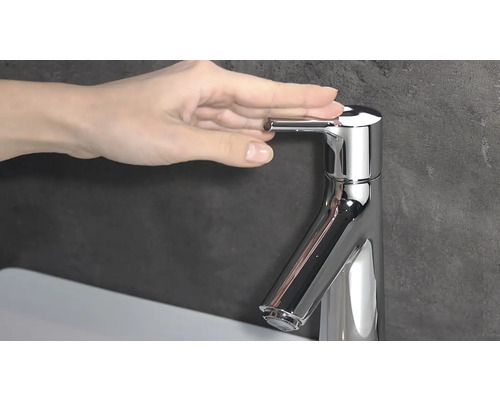 Gros plan d''un mitigeur de lavabo chromé brillant avec levier de commande et d''une main qui l''actionne.