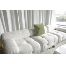 Canapé modulable blanc avec coussin et revêtement structuré devant une fenêtre avec rideaux