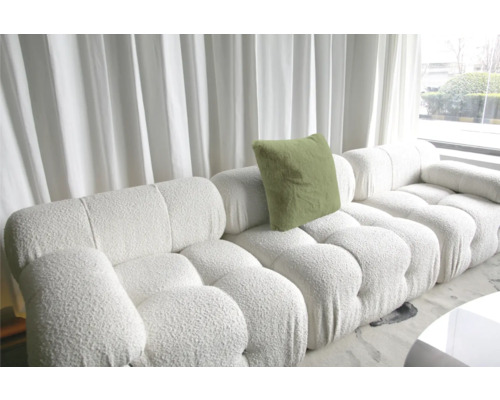 Canapé modulable blanc avec coussin et revêtement structuré devant une fenêtre avec rideaux