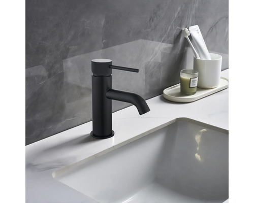 Schwarzer Waschtischmischer neben weißem Waschbecken und Badutensilien