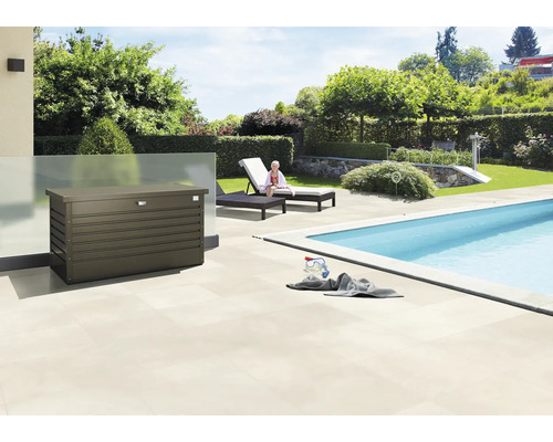 Auflagenbox Biohort FreizeitBox 130, 134 x 62 x 71 cm, bronze-metallic Szene im Freien mit einer Aufbewahrungsbox neben einem Pool, Liegestühlen und Garten.