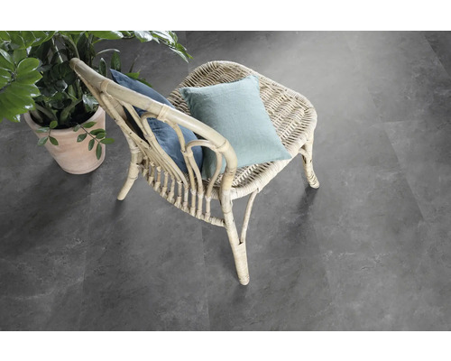 Scène avec une chaise en rotin avec des coussins et une plante en pot sur un revêtement de sol gris.