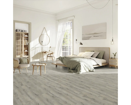 Chambre claire avec lit, chaise, table et sol stratifié imitation bois.