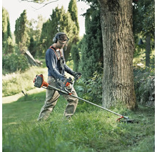 Un homme travaille avec une débroussailleuse dans le jardin et porte des vêtements de protection.