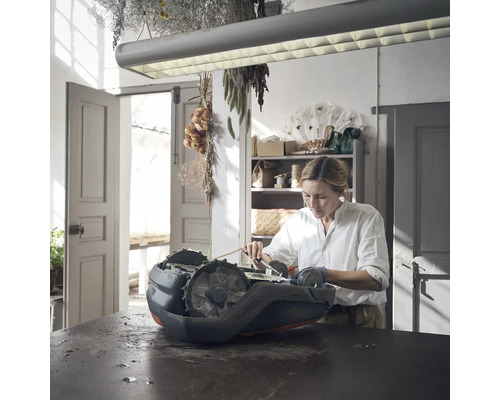 Frau reinigt Rasenmähroboter auf einem Tisch