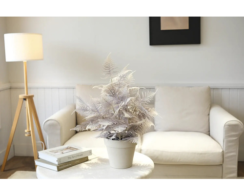 Dekorativer künstlicher Farn im Topf auf einem Tisch vor einem Sofa