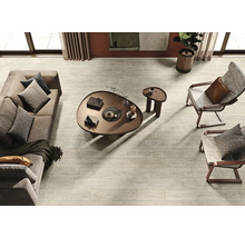 Salon lumineux avec canapé, fauteuils, table basse et carrelage de sol imitation bois.